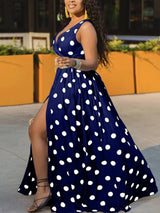 Woman wearing a navy blue polka dot maxi dress with a high slit and gold belt, shown from the side.