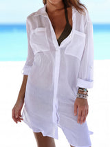 Woman wearing a white semi-sheer button-down shirt dress over a bikini at the beach.