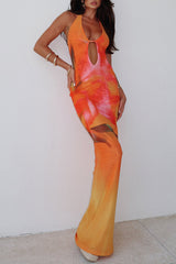 woman wearing an orange and pink floral print halter neck maxi dress with a keyhole cutout, standing against a white wall