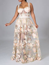 Woman in a sheer floral embroidered maxi dress with a corset-style bodice, posing against a grey background.