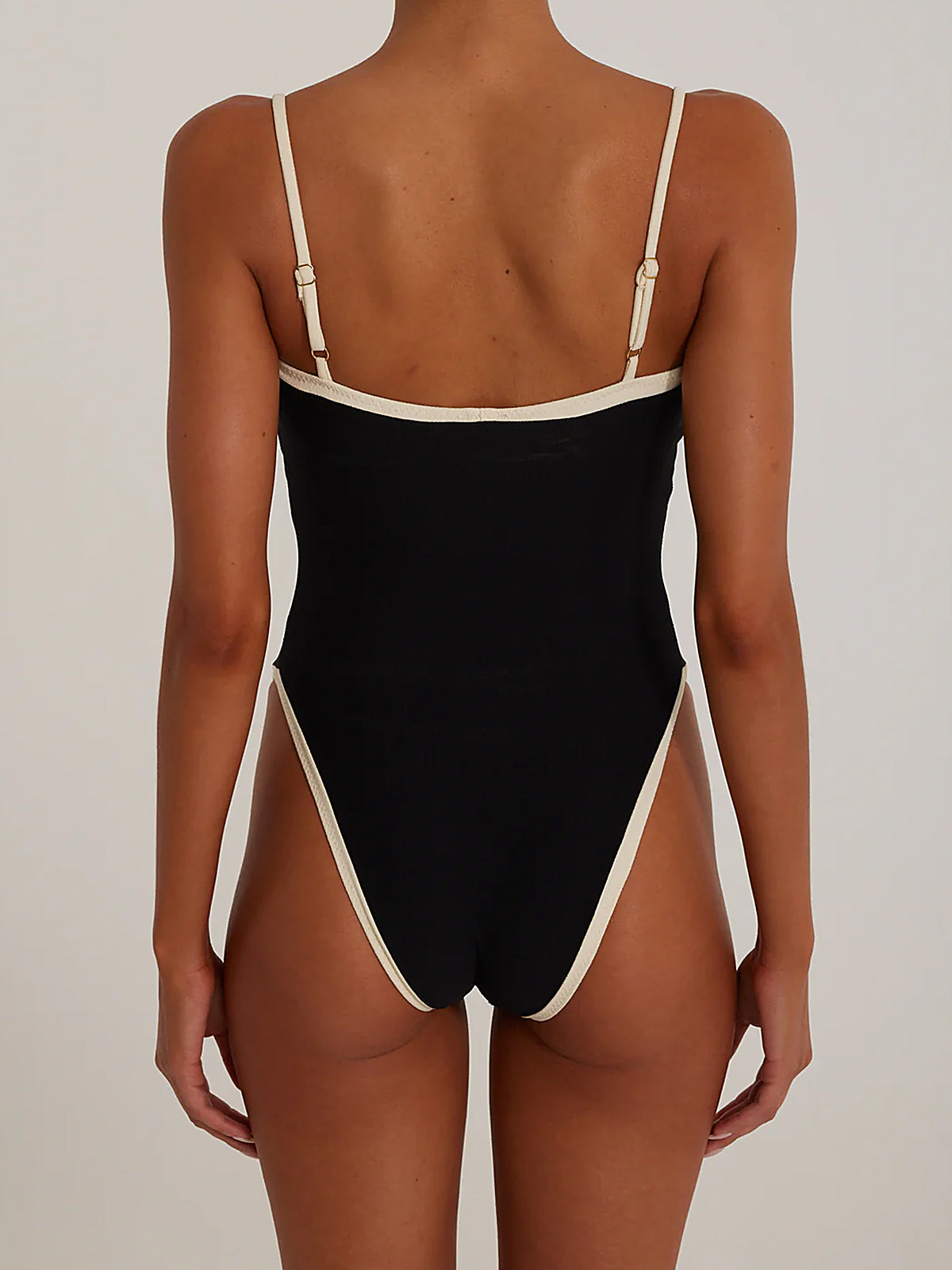 Back view of a woman wearing a black one-piece swimsuit with white trim