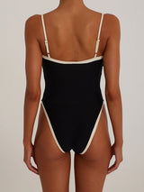 Back view of a woman wearing a black one-piece swimsuit with white trim