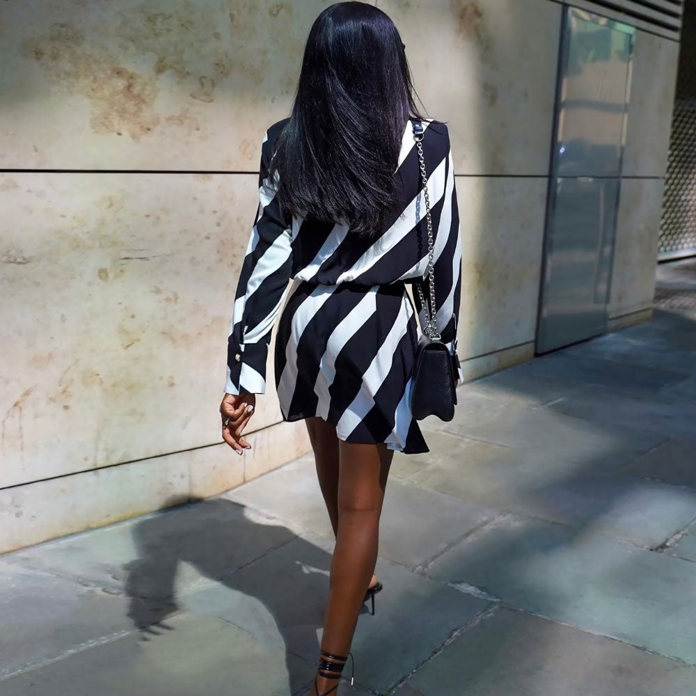 Rear view of a woman walking away from the camera, showcasing the back of a black and white striped wrap mini dress with long sleeves.