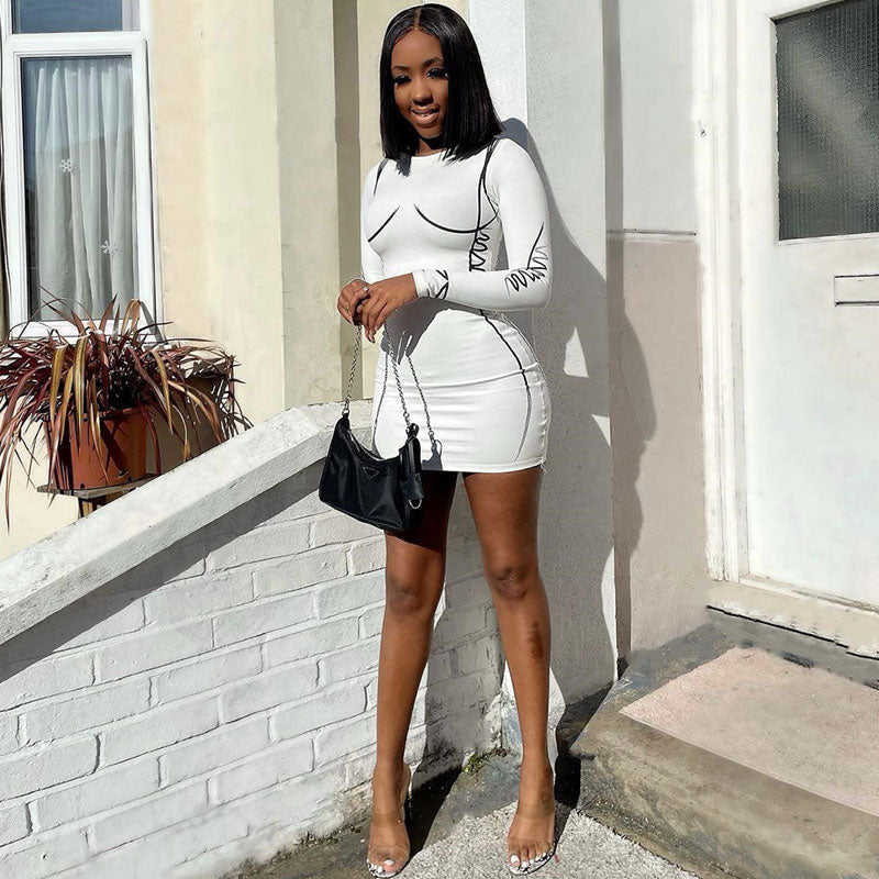 Full-length shot of a woman in a white long-sleeve bodycon mini dress with black graphic print details, standing outdoors.
