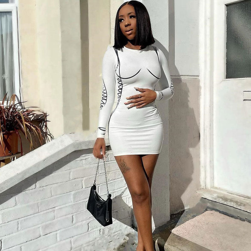 Woman posing in a white long-sleeve bodycon mini dress with black graphic print details, hand on her hip.