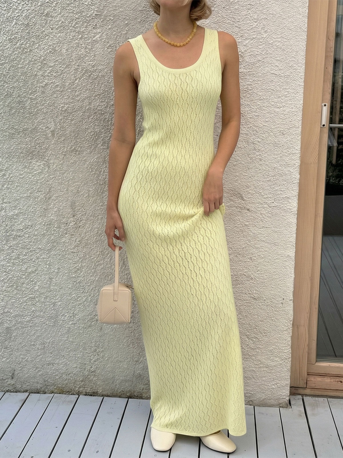 woman in a pale yellow knit maxi dress and cream shoes holding a small cream handbag