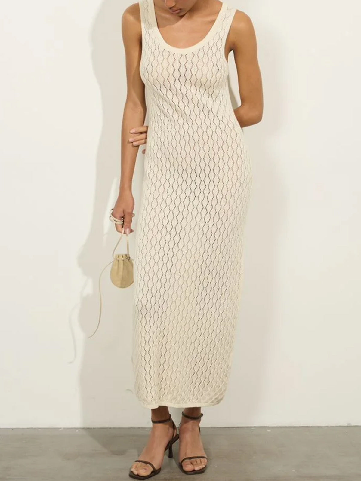woman in a cream knit maxi dress and brown strappy heels holding a small tan drawstring bag
