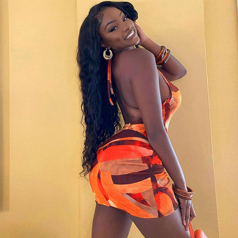 Woman posing in a short, fitted dress with an abstract orange and brown print.