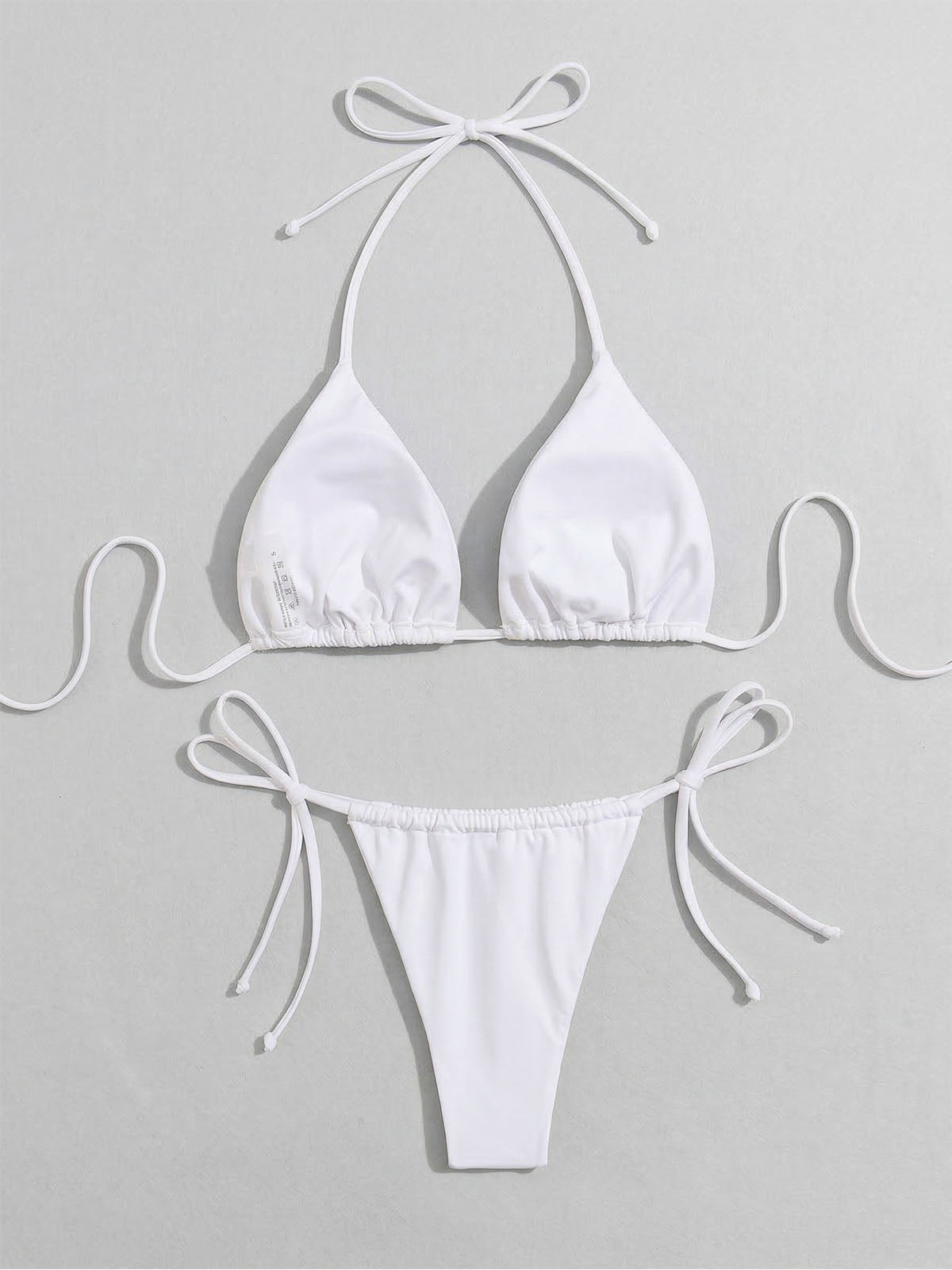 White halterneck bikini top and tie-side bottoms laid flat, detail view.