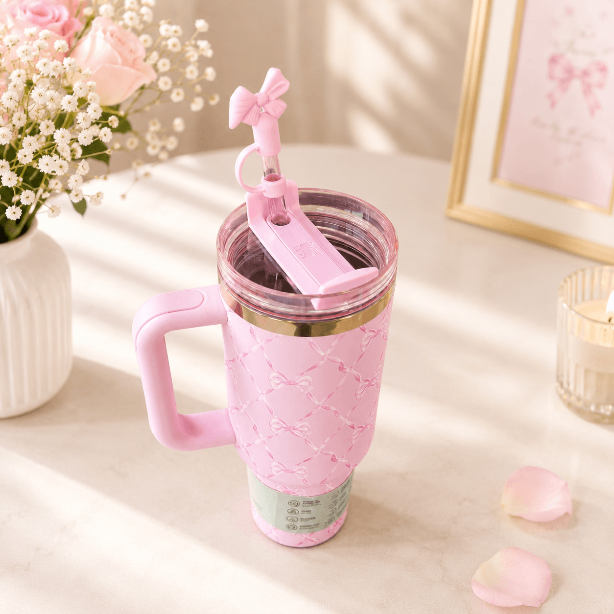 Pink travel mug with handle and straw on a light surface with flowers and decor.
