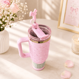 Pink travel mug with handle and straw on a light surface with flowers and decor.