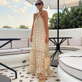 Woman wearing a cream tiered maxi dress with floral appliqué and a halter neckline, standing on a patio.
