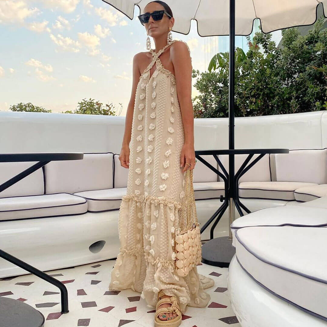 Woman wearing a cream tiered maxi dress with floral appliqué and a halter neckline, standing on a patio.