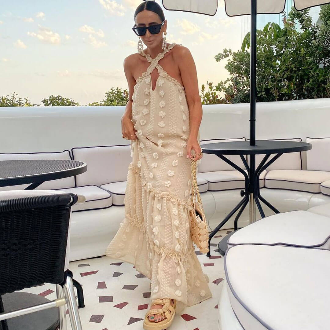 Woman in a cream tiered maxi dress with floral appliqué and a halter neckline, posing outdoors.