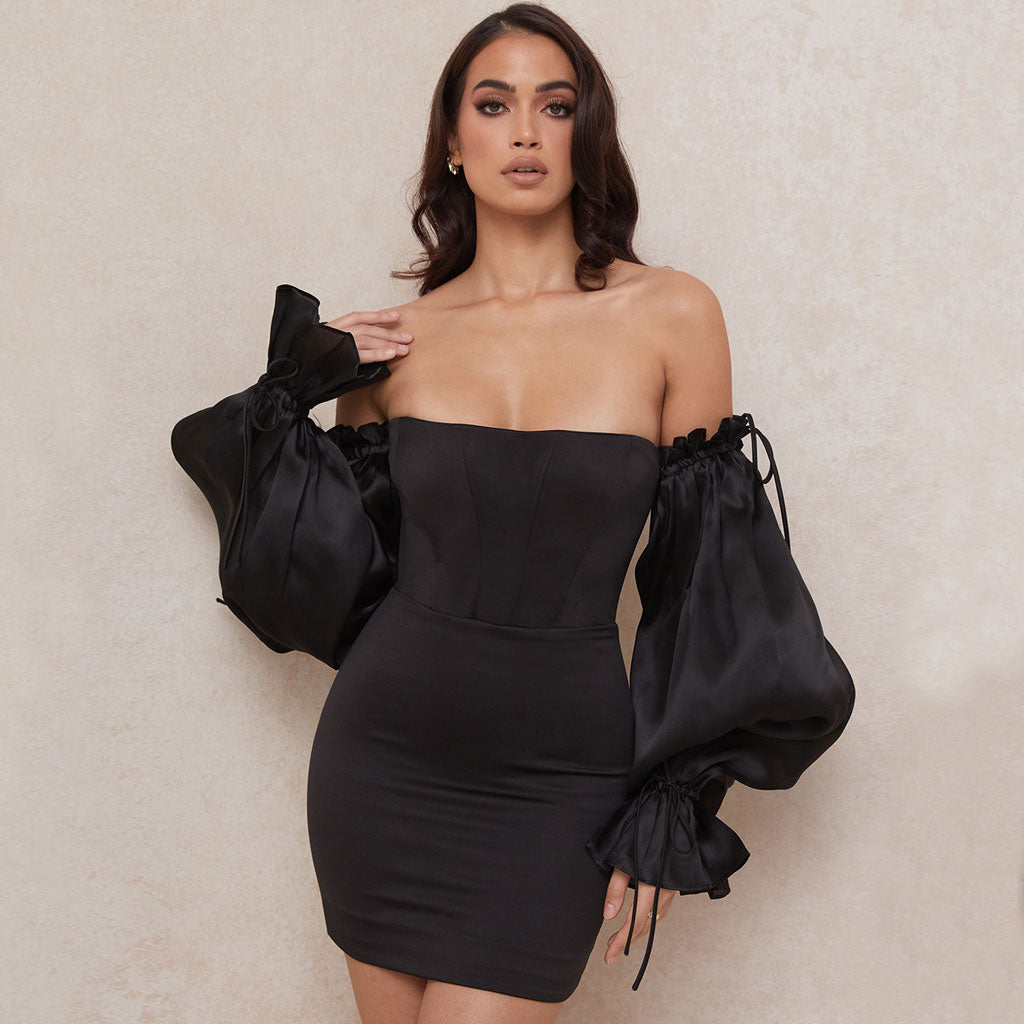 Woman wearing a black off-the-shoulder satin mini dress with dramatic puff sleeves.