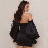 Back view of a woman wearing a black off-the-shoulder satin mini dress, showcasing the dramatic puff sleeves.
