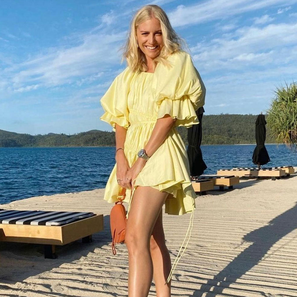 Woman wearing a yellow mini dress with puff sleeves and drawstring details on a beach boardwalk