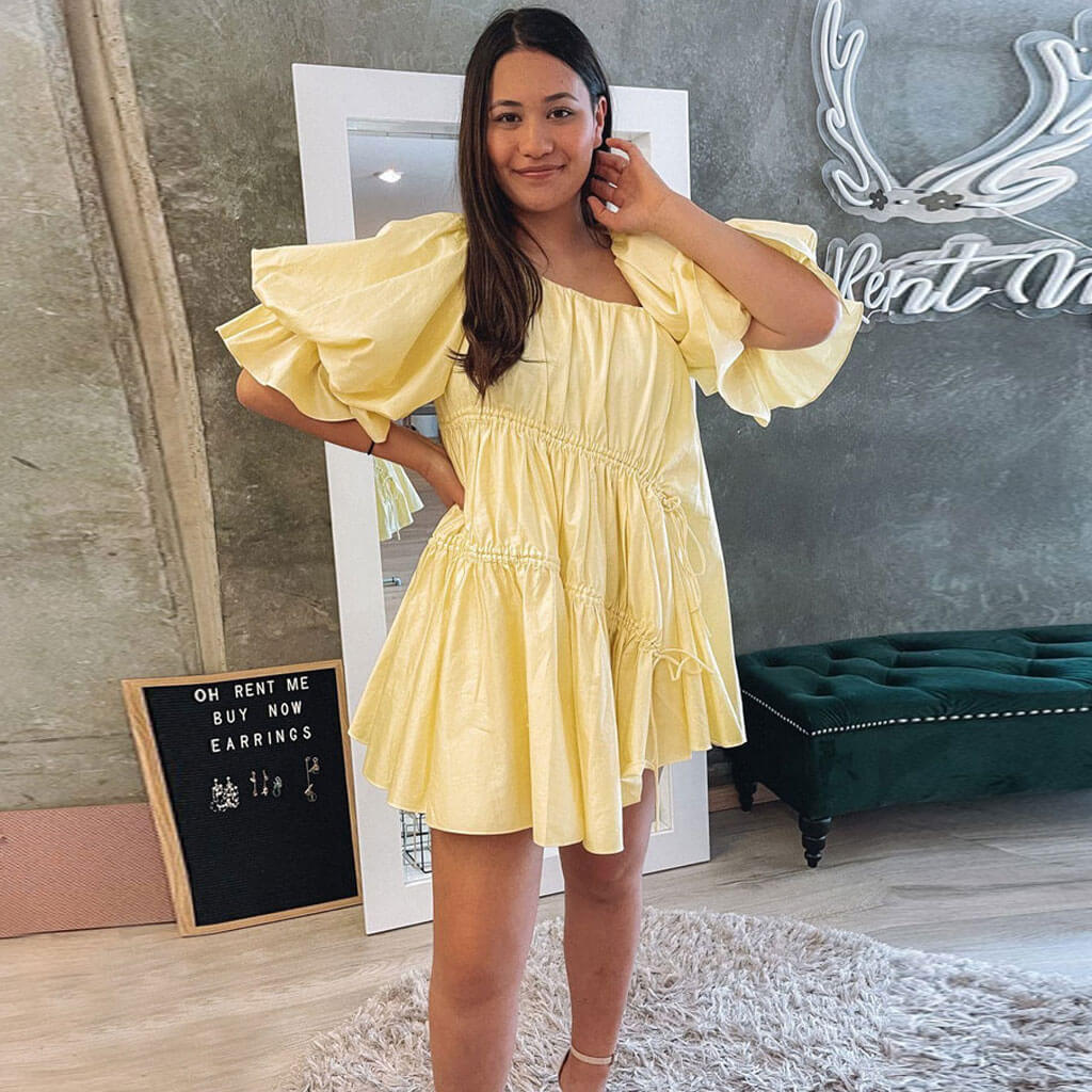 Woman wearing a yellow mini dress with puff sleeves and drawstring details indoors