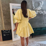 Back view of a woman wearing a yellow mini dress with puff sleeves and drawstring details indoors