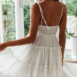 Back view of a woman in a white tiered mini dress with a smocked bodice and tie shoulder straps.