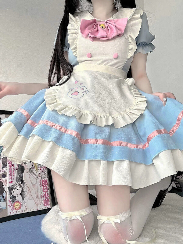 Full shot of a person wearing a blue and white maid-style dress with pink accents, standing near anime-style artwork.