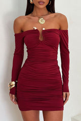 Model wearing a deep red off-the-shoulder ruched bodycon dress with long sleeves and a keyhole cutout, accessorized with gold jewelry.