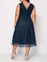 Back view of a woman in a navy blue sleeveless V-neck midi dress with sparkly embellishments and a tulle overlay.