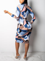 Rear view of a woman wearing a long-sleeved geometric print pencil dress with a belted waist and V-neckline, standing against a white background.