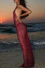 side view of a model wearing a long, sheer, red sequined halter dress on a beach at sunset