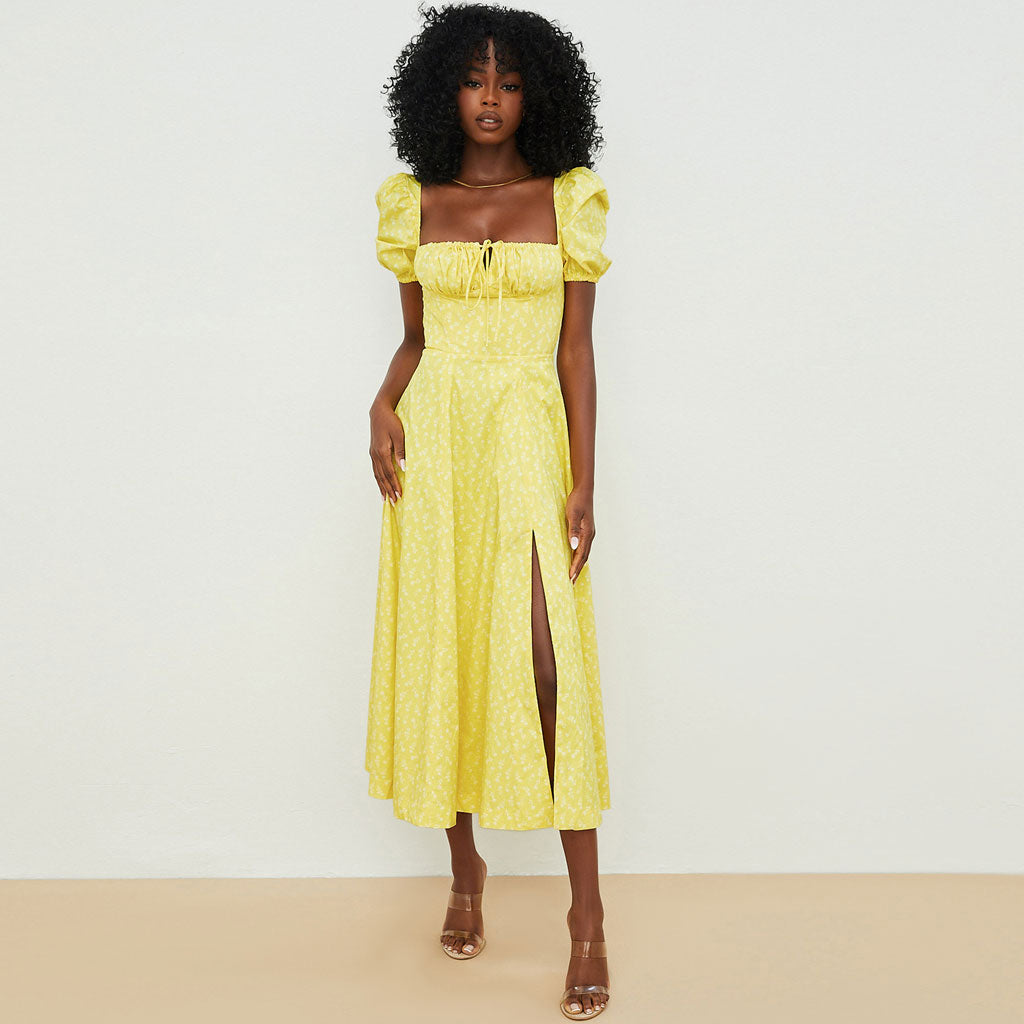Woman wearing a yellow floral print midi dress with puff sleeves and a high slit, standing against a white background.