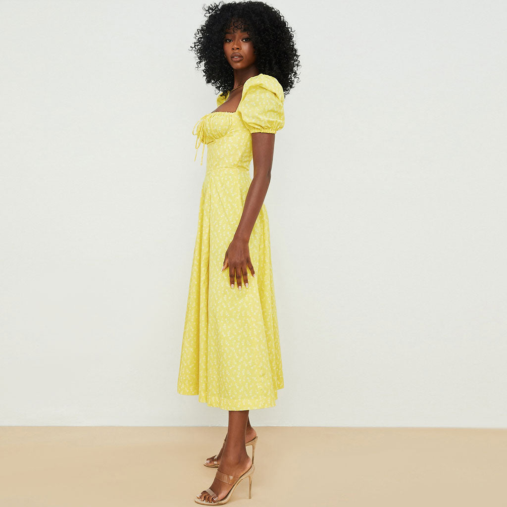 Side view of a woman in a yellow floral print midi dress with puff sleeves and a high slit.