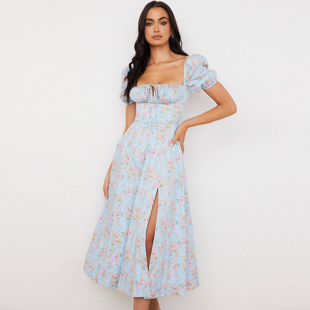 Woman wearing a light blue floral print midi dress with puff sleeves and a thigh-high slit, posing against a white background.