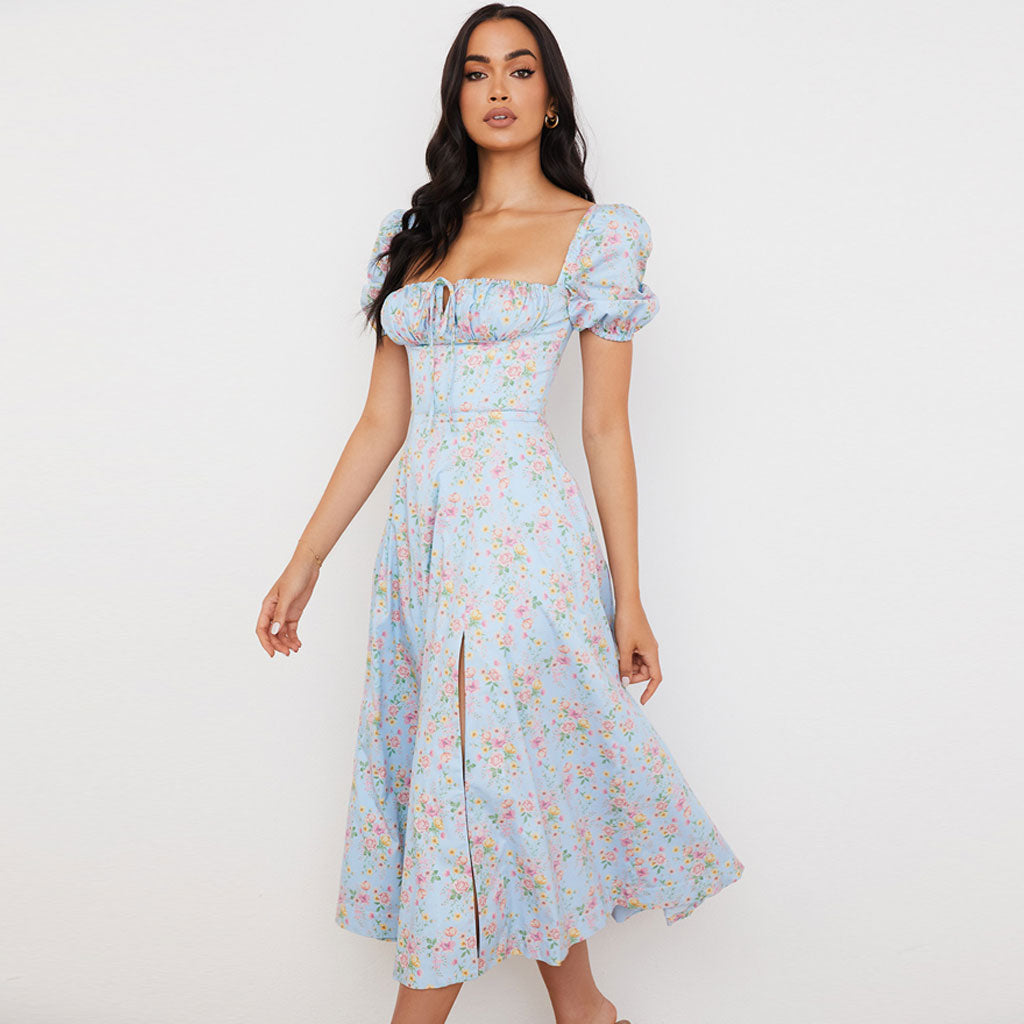 Side view of a woman in a light blue floral midi dress with a thigh-high slit and puff sleeves.