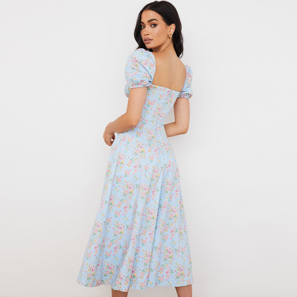 Back view of a woman in a light blue floral midi dress with a square neckline and puff sleeves.