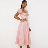 woman in a pink floral midi dress with a square neckline and puff sleeves, standing with one hand on her hip
