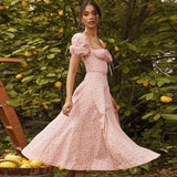 woman in a pink floral midi dress with puff sleeves and a tie detail at the bust, standing outdoors in a lemon grove