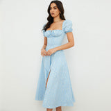 Side view of a woman in a light blue floral print midi dress with puff sleeves and a square neckline, showing a side slit.