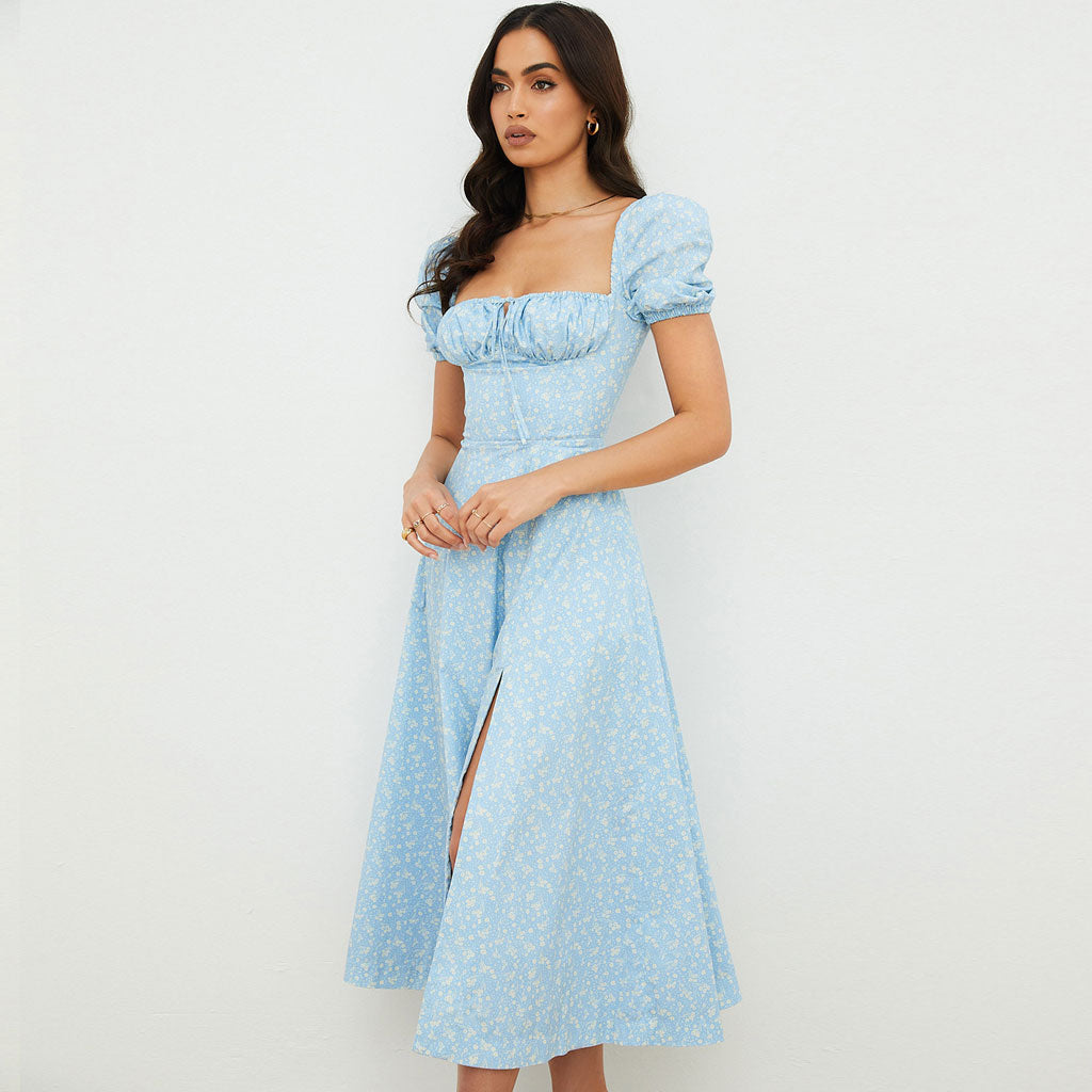 Side view of a woman in a light blue floral print midi dress with puff sleeves and a square neckline, showing a side slit.