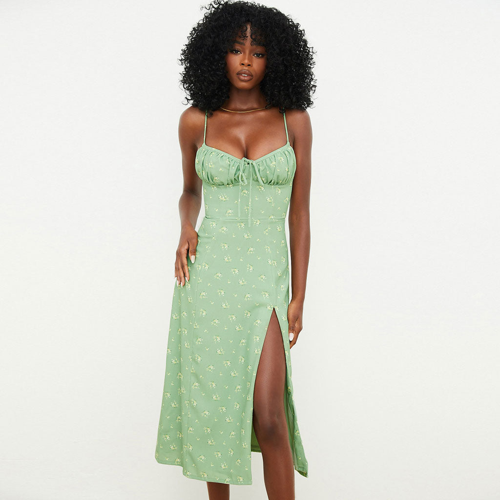 Woman wearing a green floral print midi dress with a high slit and cami straps.