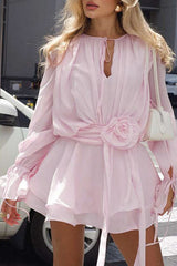 Model wearing a pink chiffon mini dress with a floral applique at the waist and ruffled cuffs.