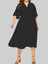 Plus-size woman wearing a black midi dress with flutter sleeves and a smocked waist, shown from the front.