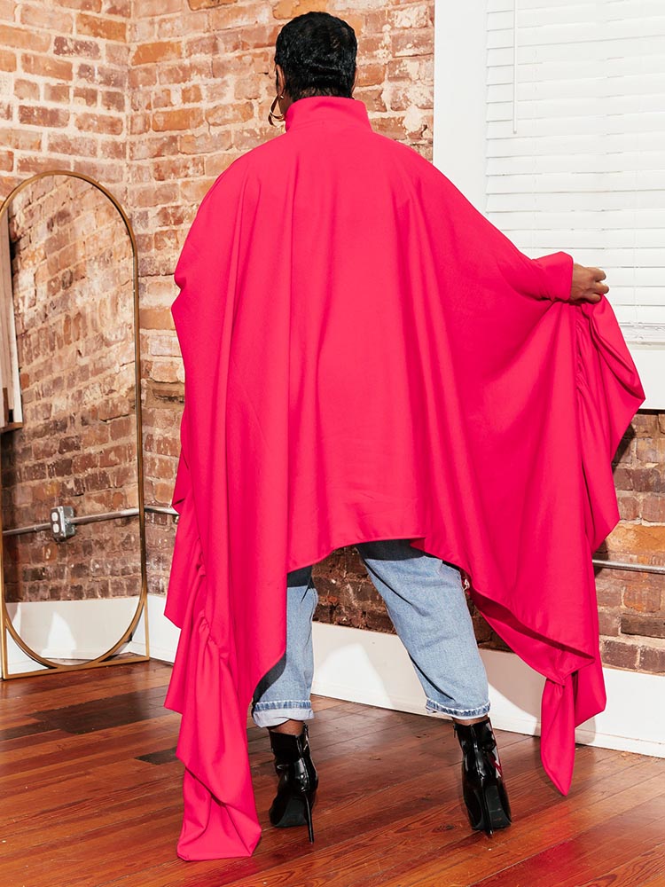 Woman wearing a bright pink oversized shirt dress over light-wash jeans, showcasing the back view with its flowing, asymmetrical design and black ankle boots.