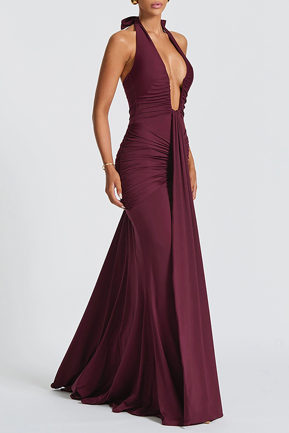 Side view of a woman wearing a burgundy floor-length halter dress with a deep V-neckline and ruched detailing.