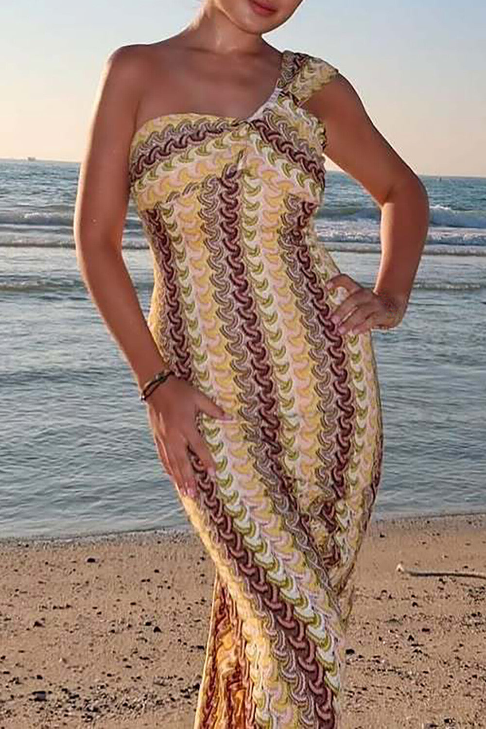 Woman wearing a yellow and brown patterned one-shoulder knit dress on a beach.