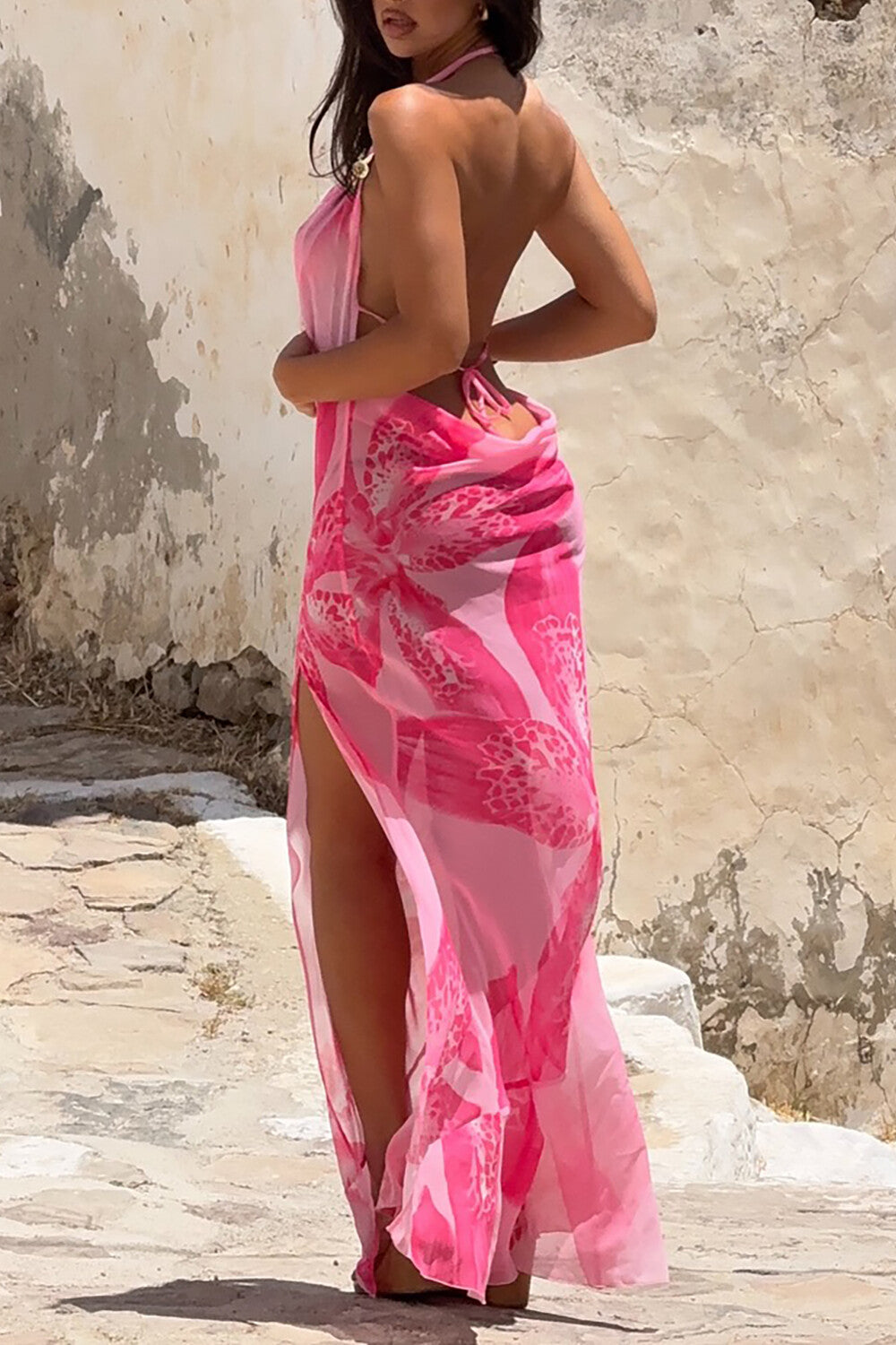 Woman wearing a pink floral maxi dress with a thigh-high slit, posing against a textured wall.
