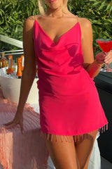 Woman in a pink mini dress with a cowl neckline and beaded fringe hem, outdoors.