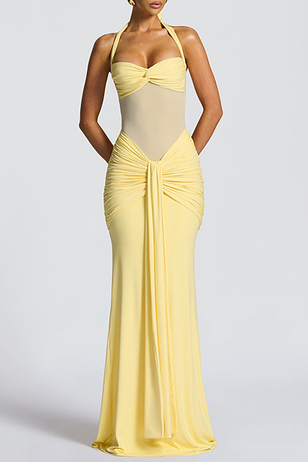 Model posing in a yellow floor-length dress with a draped skirt and halter neckline.