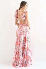 Back view of a woman in a pink floral print maxi dress, showcasing the criss-cross back detail and ruffled shoulder straps.