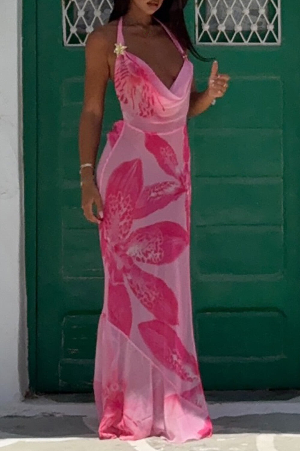 Woman wearing a flowing pink floral maxi dress with a halter neckline, standing in front of a green door.