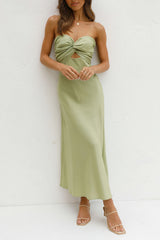 front view of a woman in a light green strapless satin dress with a twisted bust and cut-out waist, standing against a white wall